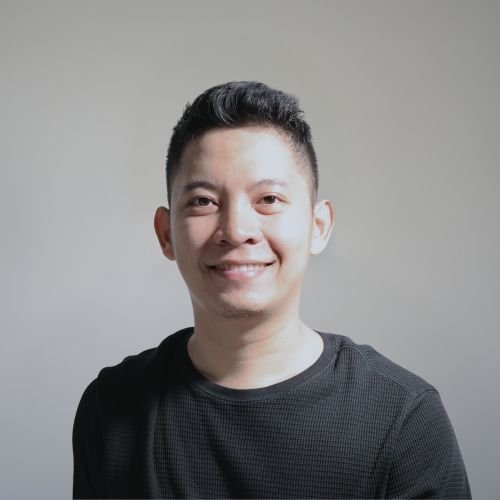 Aly, our Graphic designer, wearing a black top, smiling against a grey background.