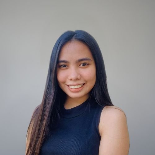 Aly, our Graphic designer, wearing a black top, smiling against a grey background.