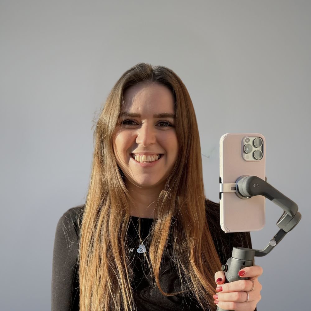 Aly, our Graphic designer, wearing a black top, smiling against a grey background.
