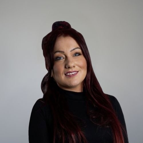 Aly, our Graphic designer, wearing a black top, smiling against a grey background.